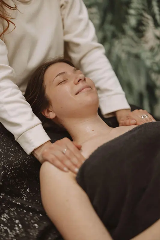 Institut-PourquoiPas_Soins_corps-01 Une femme reçoit un massage relaxant des épaules et de la nuque. Elle sourit, les yeux fermés, enveloppée dans une serviette. Le cadre est serein, avec une ambiance douce et apaisante.