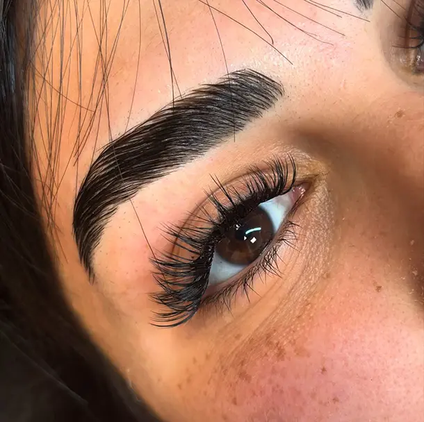 Institut-PourquoiPas_Beauté_Regard_Yumi-02 Gros plan sur l'œil d'une personne aux sourcils épais et soignés et aux longs cils. La peau a une texture naturelle et le regard paraît brillant et précis.